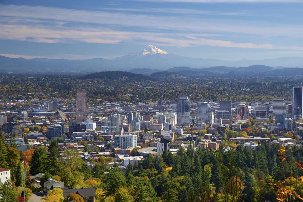A panoramic view featuring the downtown skyline, Mount Hood in the distance, and lush, leafy greenery filled with autumn hues. The expansive vista hints at the variety of parks, trails, and greenspaces available for exploration near Bridlemile Cottage.