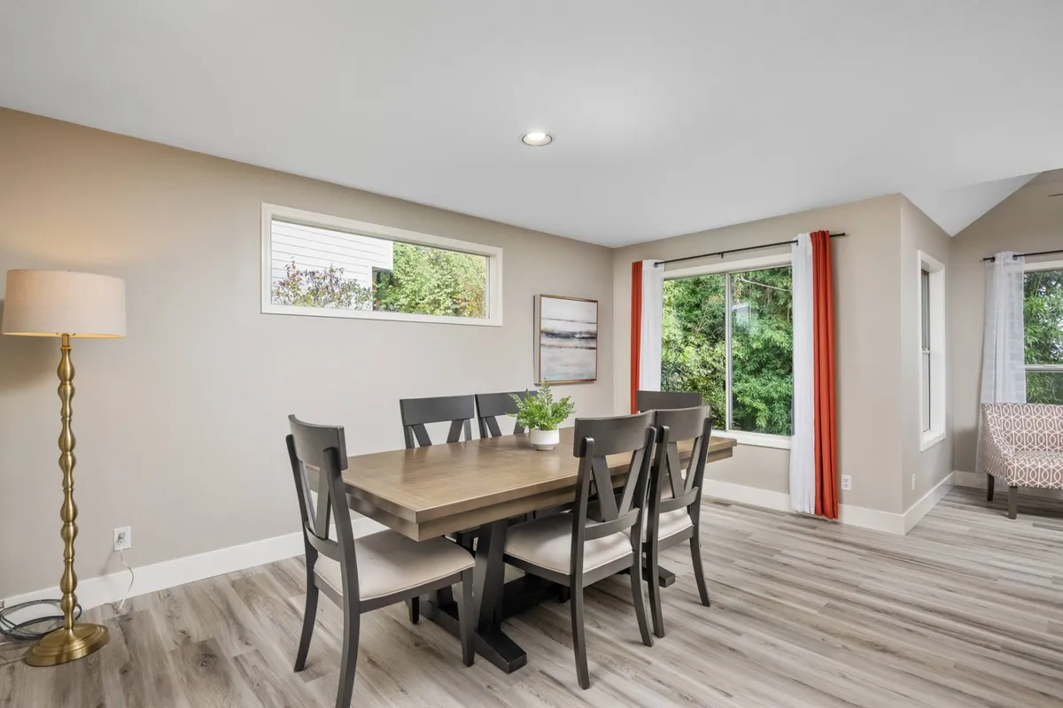 This interior photo centers on a dining table set near large windows, bathed in cozy lighting, and accented by warm artwork. It radiates a sense of togetherness, social gatherings, and game nights, echoing the activities described for the garage entertainment space.