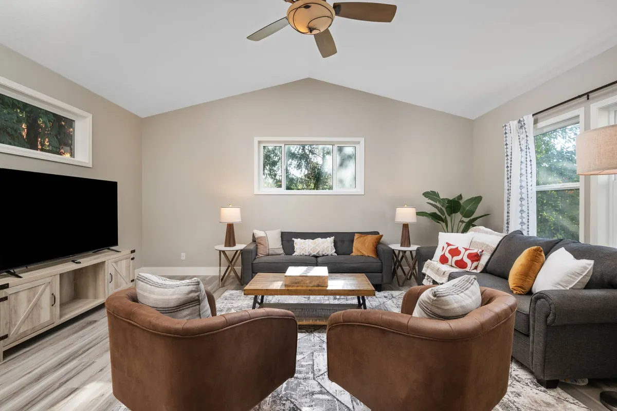 The hero image showcases a warm, inviting living room featuring a plush sofa, stylish armchairs, a modern coffee table, and large windows that fill the space with natural light. The setup is perfect for relaxing, enjoying movie nights on the television, or gathering for cozy conversations. Subtle touches like tasteful decor and soft lighting create a comfortable, family-friendly atmosphere.