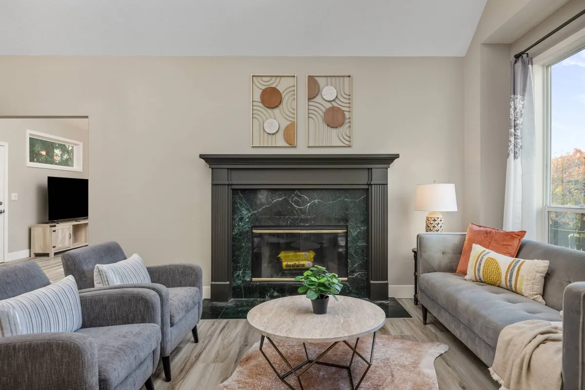 A close-up of a cozy sitting area with a soft sofa, a stylish coffee table, and a fireplace as the focal point. The window brings in natural light and frames outdoor greenery, while the overall look is intimate and perfect for either solitude or close company.